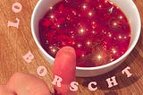 A bowl of borscht with my thumb next to it. The thumb has stained lines.