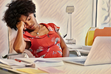 A creative writer appearing to be suffering from burnout and mental exhaustion sits behind a laptop. She is a black woman holding her head in her hand. She seems as if she isn’t inspired. The image represents lack of inspiration and productivity.