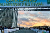 Starting line of a marathon, with the banner “Oakland Running Festival” and a sunrise-lit sky in the background