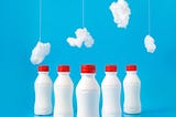 white bottles with red caps lined up against a blue background with white cotton batting dangling above