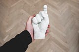 A hand holding a white statue with the shape of a hand pointing towards the reader