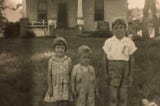 Black and white photo of three children posed in front of a house