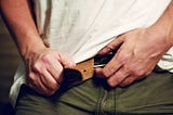 A man, tightening the belt on his trousers.