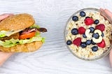 Image of one hand holding a burger and the other hand holding oatmeal with berries