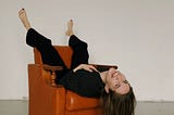 Woman in suit laying upside down on a brown sofa, laughing