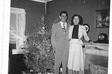 A black and white photo of a man and woman on their wedding day in 1953. There’s a Christmas tree in the background.