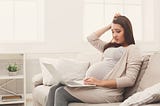 Pregnant woman reading something embarrassing on a laptop