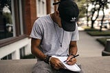 A man sits on a ledge outside and writes in his notebook.