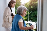 Women looking outside their window, holding cups of tea