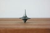 Silver metal top spinning vertical on a wooden table with a white background.