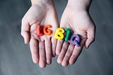 A person holding the letters “LGBTQ” made in colorful playdough.