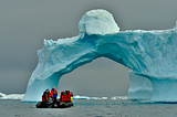 A boat beneath an iceberg’s arch, hinting at the vast hidden bulk, much like the pivotal, untested sliver in software’s depth.