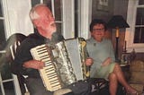 Man playing the accordion and singing with woman sitting beside him