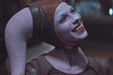 Natalie Tena as Xi’an, smiling to reveal sharpened incisors that resemble fangs