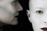 A human or human-like figure appears to whisper something into another human’s ear.