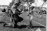 Photo no 127-GW-090935, July 1944 “Give me candy.” Photo of soldier giving candy to child in Tinian.