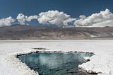 a spring of water in a desert, possibly salt, blue sky and white clouds