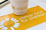 Image of a bucket and poster with a white and yellow Cancer Fund For Children logo