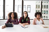 Three women sitting in an office in disbelief