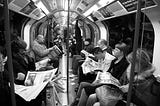 Black and white photo of a tube carriage filled with people sitting and reading newspapers