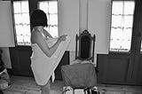 black & white photo of a woman wrapped in a towel standing over an open suitcase