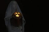 a spooky dark picture of a young girl in a ghost costume holding a lit jack-o-lantern