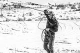 Black and white photo of man twirling a lasso in snow-covered Wyoming.