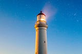 A lighthouse shines bright toward a sky of stars.