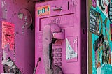 An old payphone that is spray-painted pink with grafitti and stickers all over it.
