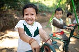 A young Thai girl is wearing a green and white shirt and playing on a playground with several other children.