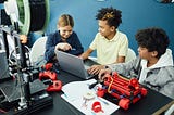 Students work together on solving problem with a computer and brightly colored robotic devices on a table top.