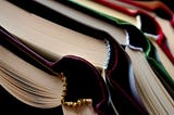 stack of rainbow-colored books, spines forced open, maybe on a discard pile