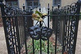 The grave of Joseph Grimaldi. A weathered headstone and grave is surrounded by black, ornate, cast-iron railings. The twin masks of tragedy and comedy — also in black iron — hang on the railing.