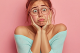 article key visual with a young woman with glasses, looking nerdy, showing a strong emotional pain, demonstrating a recent pain, feeling painful. Key colors “e11a72. Studio shot, hyper-realistic, photo realistic, canon D118 shot,, flat pale pink background,