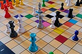 The White King checkmated by a Slate Queen and surrounded by Cyan, Ash, and Black Queens.