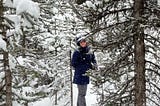 Leigh-Anne is standing among snow covered pine trees.