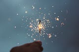 The silhouette of a hand holding a sparkler against a mid to dark blue background