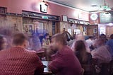 A slightly blurred picture showing a crowd of people seated in a pub.