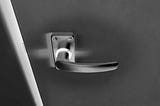 A black and white photo, with inverted colours, showing a door handle of a door that is slightly open.