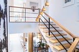 A white room with wooden accented stairs leading down to a sitting room below.