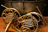 A timpani drum and sticks with two French horns poised in front.