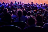 view from behind of people sat in a theatre waiting for a performance to begin