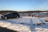 tesla model sits on snow ground in campground near lake