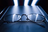 Close up of thin black eyeglasses frame on a dark blue surface with LED lights in the back.