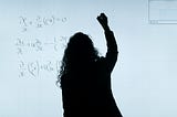 woman standing at white board writing out a formula with a marker