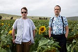 Die Herausgeber von The Quietus, Luke Turner und John Doran, stehen in einem Sonnenblumenfeld.