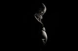 Pregnant young woman looking down at her bump which she is cradling with her hands.