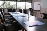 An empty corporate meeting room, looking down the length of the table. Files and bottles of water have been placed on the table at each seat, ready for a meeting.