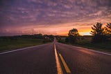 An empty road in between grass fields at dusk