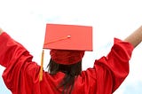 a persona in the graduation cap and gown faces away from the camera with hands and arms up in the air in celebration